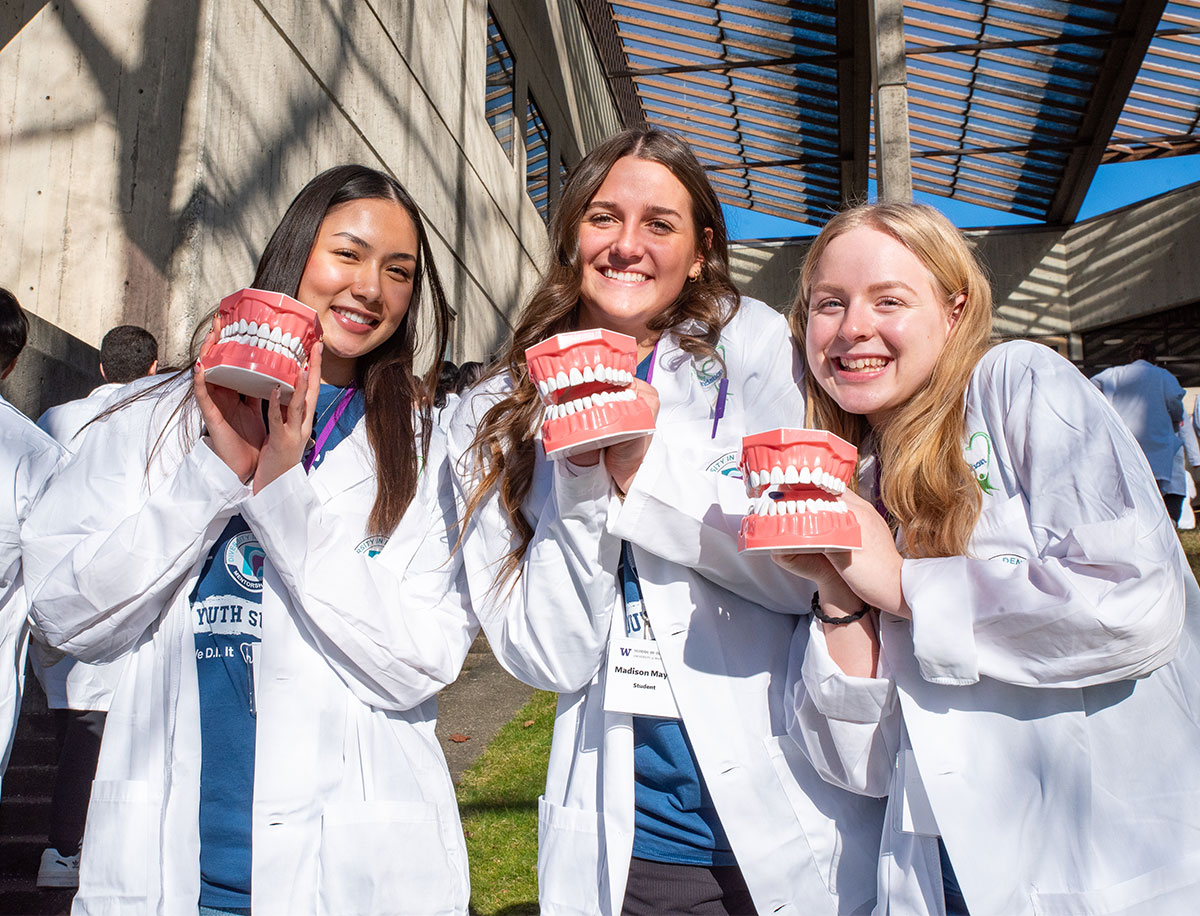 three dental academy students in white coats holding teeth molds